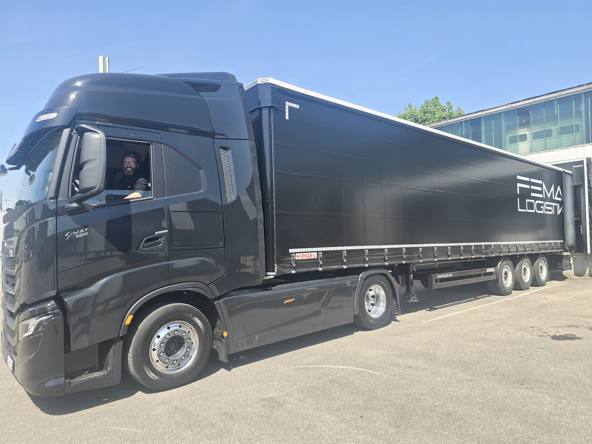 Schwarzer FEMA-Sattelzug (IVECO S-Way mit KÖGEL-Auflieger) und Fahrer im Fahrerhaus